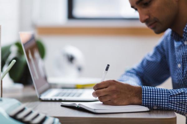 Man writing next to laptop